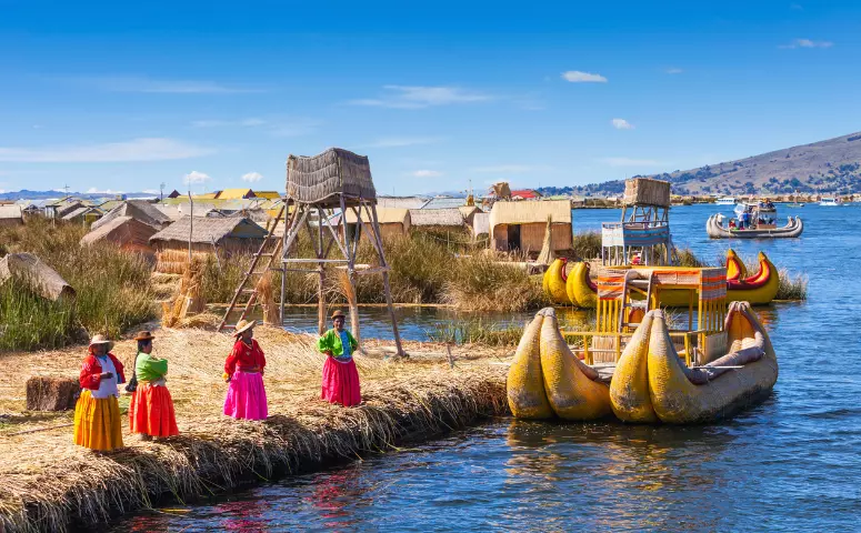 Lugareños en traje típico sobre isla flotante y bote antiguo en el lago Titicaca con Exploor Peru