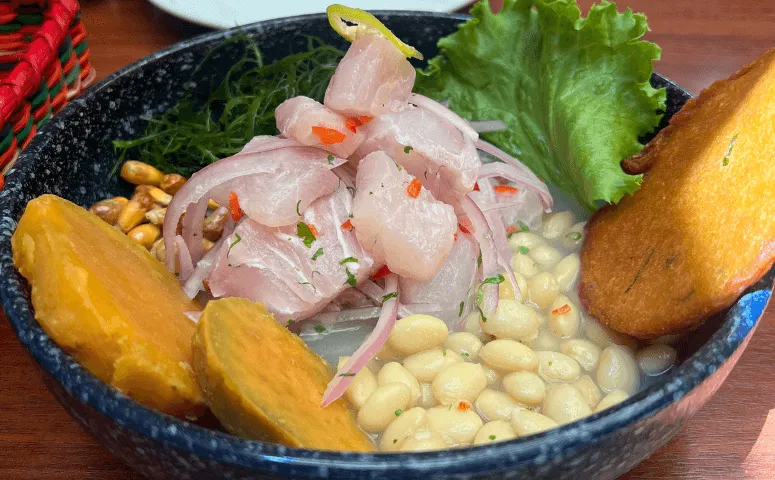 Pescado blanco crudo con maiz, camote y hierbas en un tazon negro. 